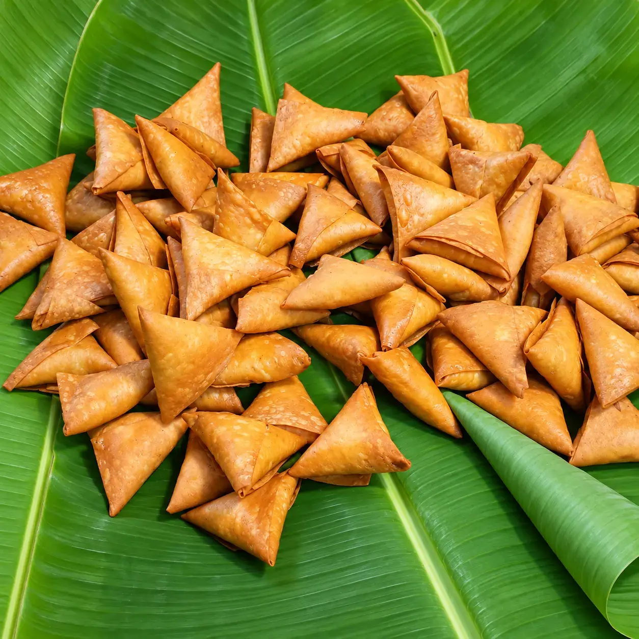 A generous serving of crisp golden samosas arranged on banana leaves