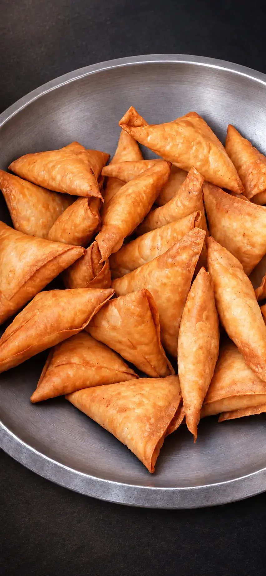 Crisp golden samosas piled in a round stainless steel serving tray
